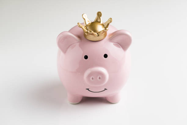 King of money savings concept, financial winner, smiling happy pink piggy bank wearing a golden crown on seamless white table background, bright future of compound interest investment stock photo