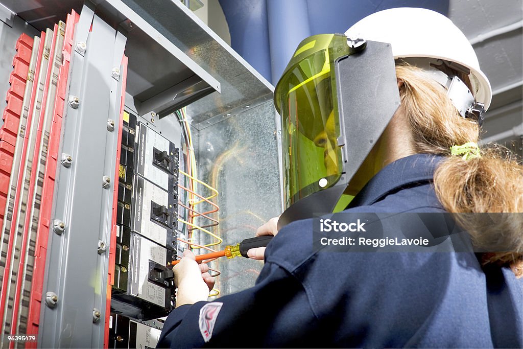 Female Electrician Female Electrician with arc flash protective clothing performing work in an energized panel with a happy smile. All trade marks removed or modified Arc Flash Stock Photo