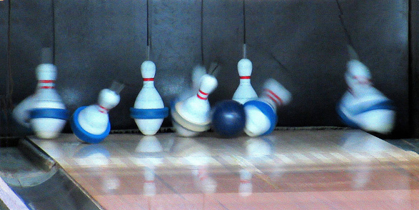 Abstract...This long, horizontal image, shows the moment of impact, of a bowling ball against pins in a bowling lane. This is not a crisp image but is interesting for it's blurred motion of the flying pins.