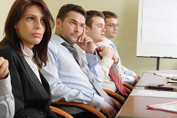 Group of men and women sitting at a desk looking bored stock photo
