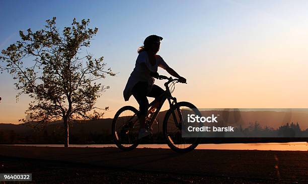 Silhouette Of A Girl Riding A Bike Along A River Stock Photo - Download Image Now - Active Lifestyle, Activity, Adult