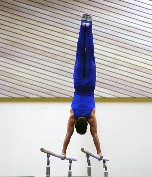 A male gymnast in a blue outfit working the bars at the gym stock photo