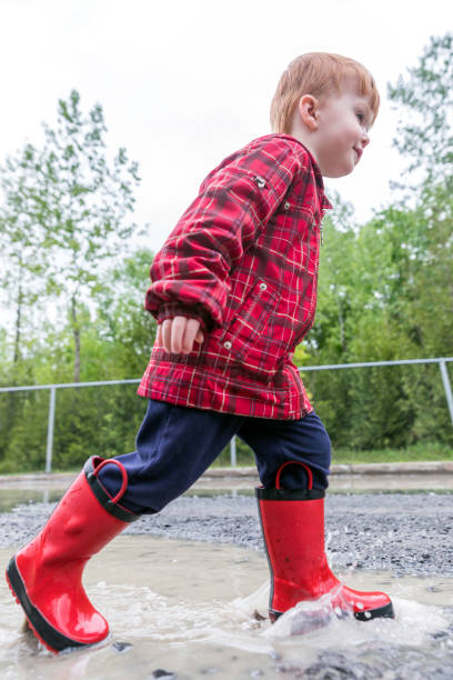 istock Young Cute Kid Walking Jumping into Water Puddle 964010756