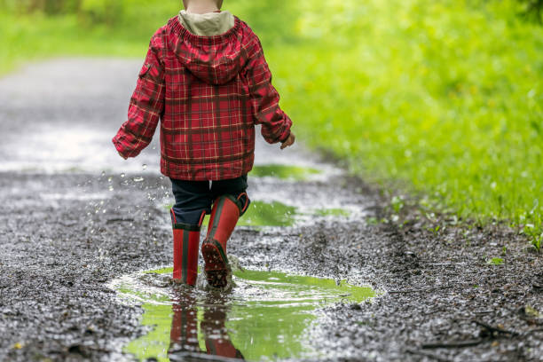 istock Young Cute Kid Walking Jumping into Water Puddle 964010774