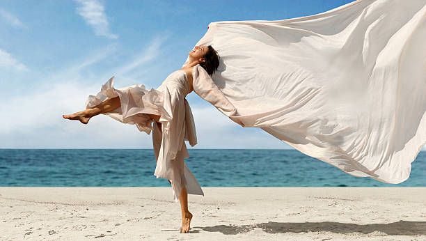 istock Happy woman dancing with blowing fabric on the beach 96403355
