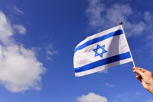 Woman wave flag of Israel against blue sky and white clouds on Israels 70s independent day.