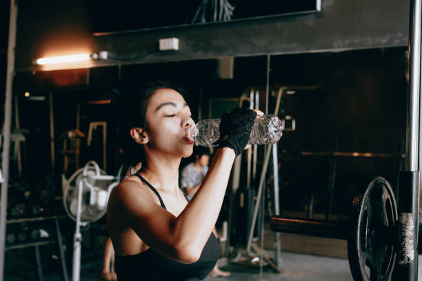 asiatique jeune femme l’eau potable dans le gymnase. - aerobics beautiful bottle body photos et images de collection