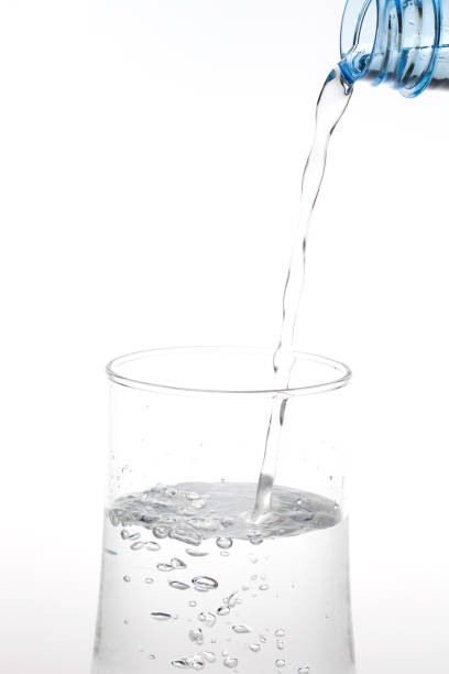 istock Pouring water from bottle into glass on white background. 964085006