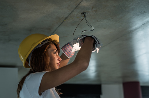 Female electrician tightening light bulb during home renovation process.