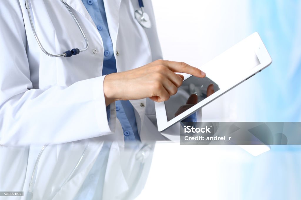 Woman doctor using tablet computer while sitting. Reflecting glass table is a working place of physician. Healthcare, insurance and medicine concept Woman doctor using tablet computer while sitting. Reflecting glass table is a working place of physician. Healthcare, insurance and medicine concept. Doctor Stock Photo