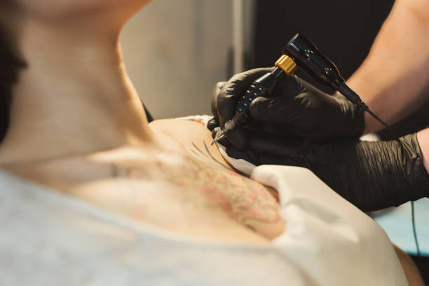 Tattoo artist working with needle on clients body Concentrated tattoo artist working with needle on clients shoulder, making popular body modification for young woman in studio, copy space shoulder tattoo designs for men stock pictures, royalty-free photos & images