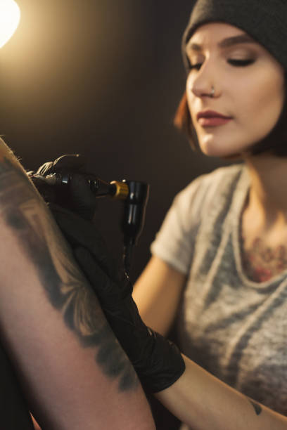 Concentrated woman tattooist doing tattoo with tattoo machine on male shoulder. Unusual female profession, copy space