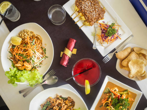 Overhead view of Thai food laid out on a white table with a dark brown runner