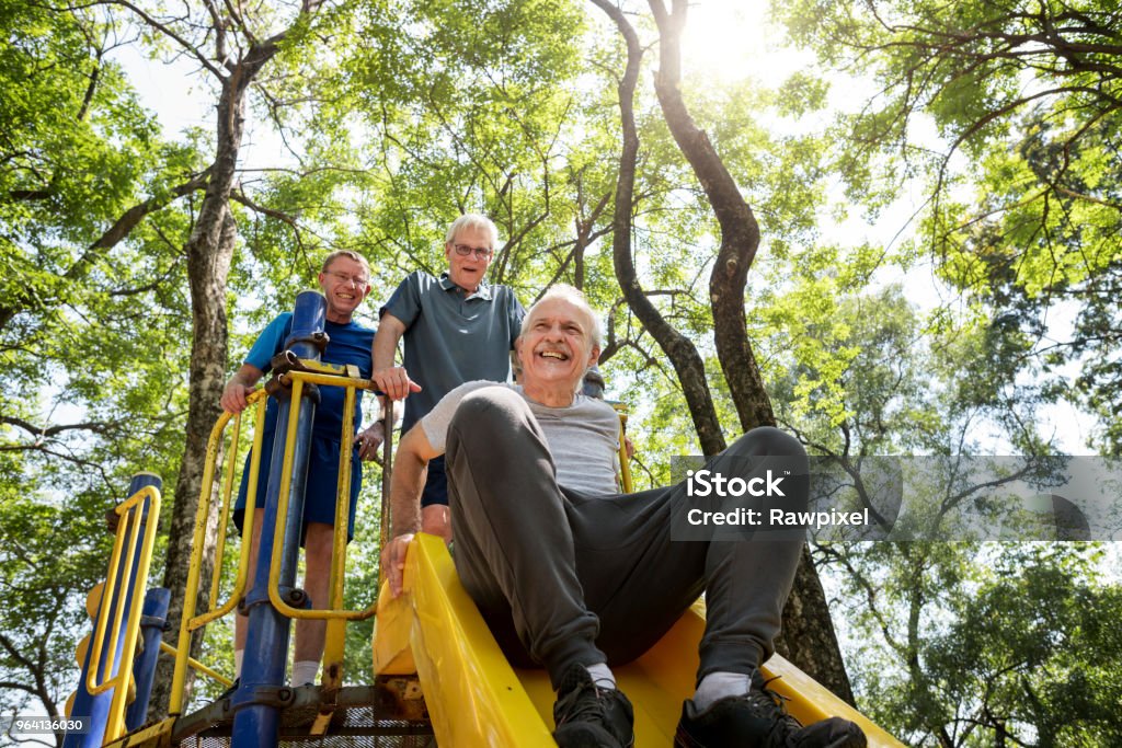 Senior men playing at a playground slide Senior Adult Stock Photo