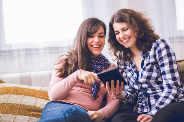istock Two women laughing while sitting on the couch together and looking at the tablet. 964147138
