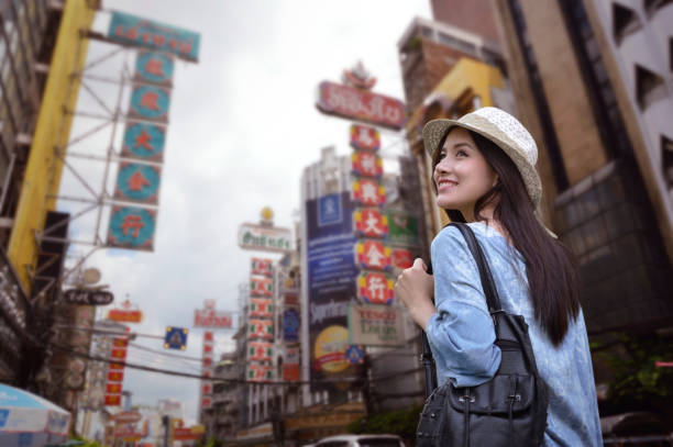 Young asian woman traveler with a backpack on her shoulder and travel hat walking on footpath over China town, Bangkok, Thailand, Travel holiday relaxation concept stock photo