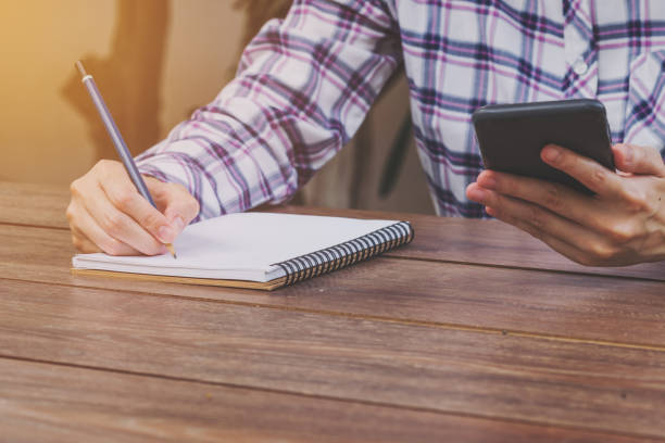 istock Hand woman holding phone and writing notebook on wood table with cup coffee. 964148166