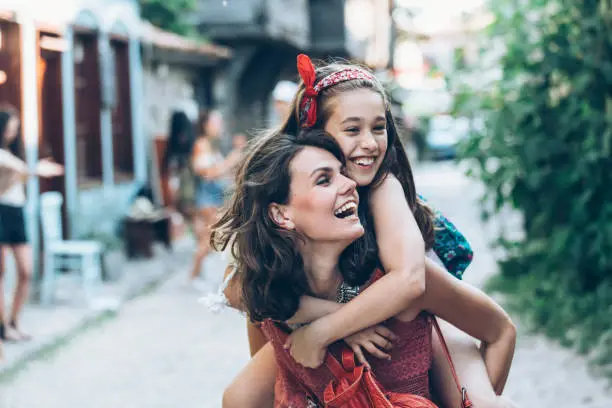 Mother and little girl having fun in piggyback ride outdoors.