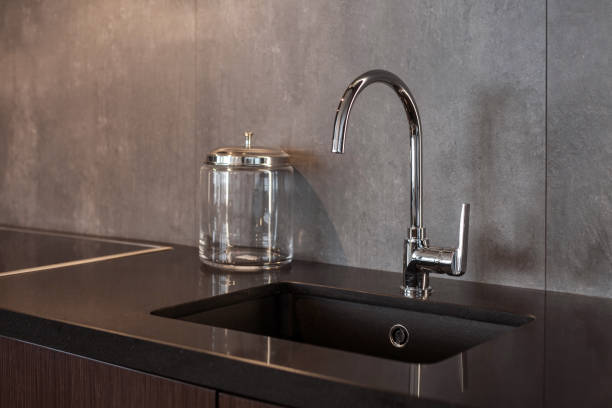istock Detail of a rectangular designer kitchen sink with chrome water tap against a gray textured wall 964155660