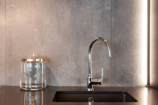 istock Detail of a rectangular designer kitchen sink with chrome water tap against a gray textured wall 964155690