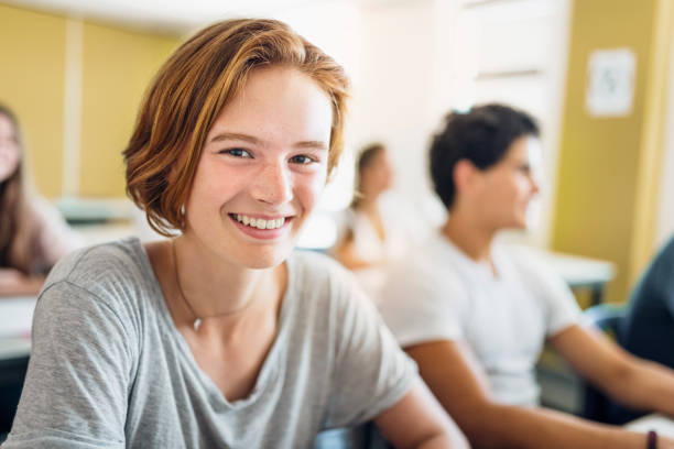 Portrait of female student smiling in classroom Portrait of female student smiling in classroom. Confident learner is wearing casuals. Teenage girl is with short brown hair. Feminine Boy in High School stock pictures, royalty-free photos & images