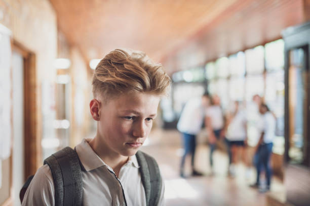 Student being bullied by classmates in school Teenage student being bullied by classmates in school. Sad boy is looking away. University students are making fun of him in corridor. exclusion group of people separation fish out of water stock pictures, royalty-free photos & images