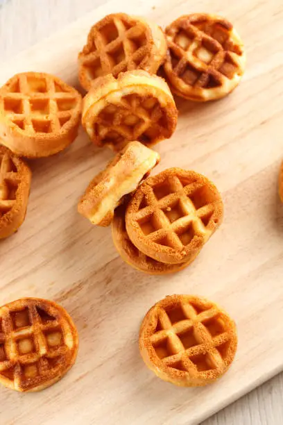 Photo of circle mini waffles on wooden cutting board. Top view