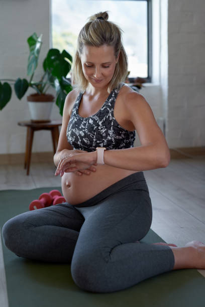zwangere vrouw horloge kijken terwijl het aanraken van de buik na het sporten - pregnant count stockfoto's en -beelden