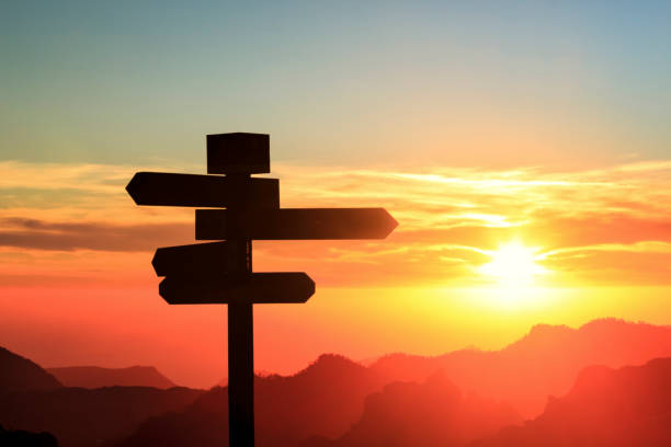 Silhouette of a signpost in a colorful sunset Silhouette of a sign with four directions with mountains and sunset in the background crossroad stock pictures, royalty-free photos & images