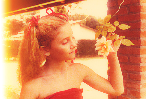 Vintage image from the seventies featuring a girl holding a rose flower outdoors.