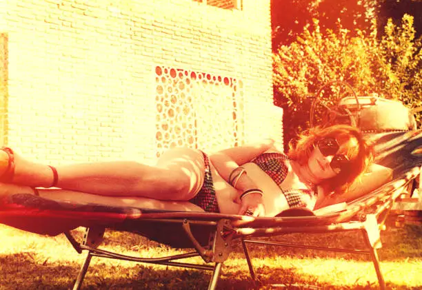 Vintage image from the seventies featuring a fashionable woman reading and relaxing in a lounge chair outdoors.