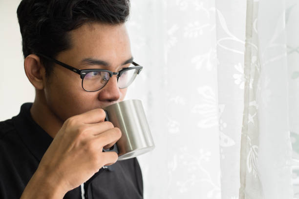 istock Young Man Holding Cup While Standing By Curtain At Home 964194764