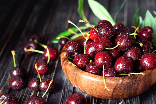 Fresh sweet cherries in plate on dark wooden background with copy space. Summer and harvest concept. Cherry macro. Vegan, vegetarian, raw food.