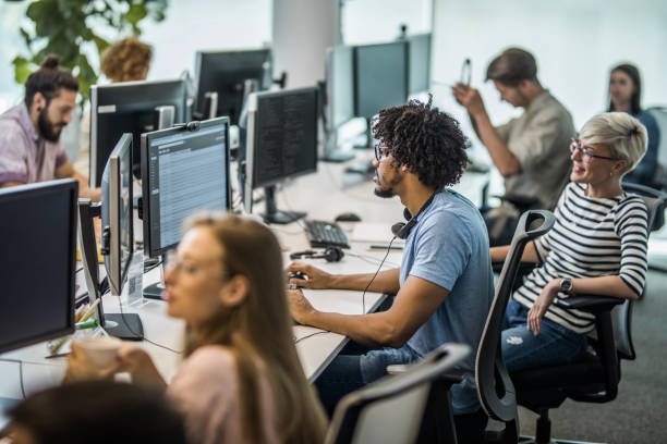 istock African American programmer working on desktop PC in the office full of people. 964216144