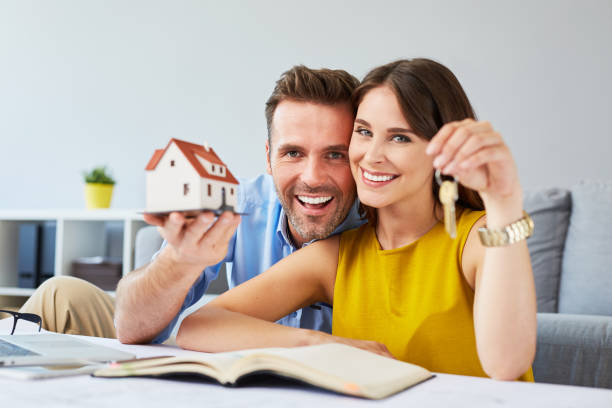 Happy couple holding keys to new home and house miniature stock photo