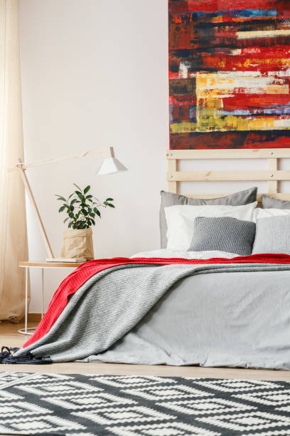 istock Painting above bed with red and grey sheets in bedroom interior with patterned carpet. Real photo 964254278