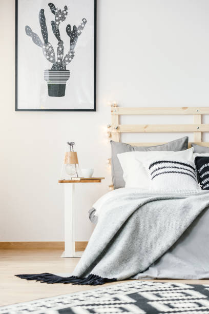 istock Cactus poster on white wall above bed with grey sheets in bright bedroom interior. Real photo 964254426