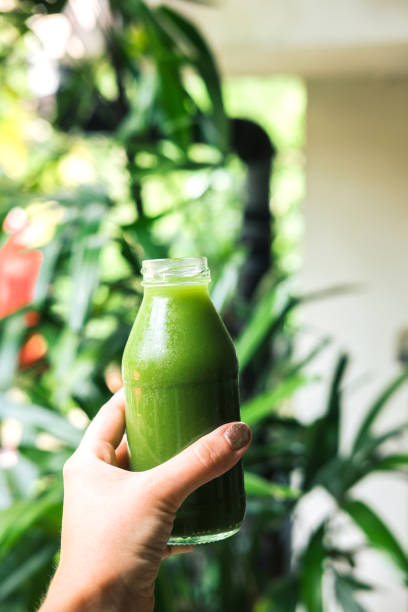 Woman's hand holding a bottle with green juice, nature background. Healthy eating, detoxing, juicing, fasting, body cleancing concept