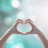 Healthy human hand in heart shape showing love friendship on blurred abstract cool blue green sky color bokeh background: Global eco environment CSR natural resource awareness/ concept/ campaign/ idea