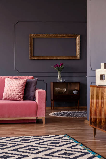 istock Empty gold frame hanging on wall with molding above retro cupboard with fresh purple tulips in glass vase 964263846