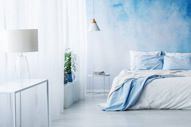 istock White lamp on a table in bright blue bedroom interior with bed against ombre wall 964266906