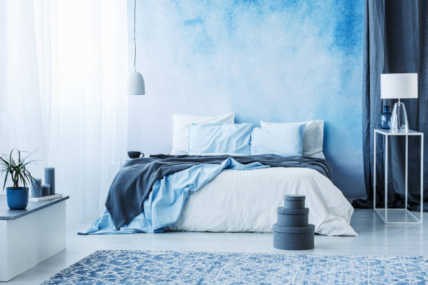 istock Grey boxes next to bed with blue bedding in bedroom interior with white lamp against a curtain 964266944