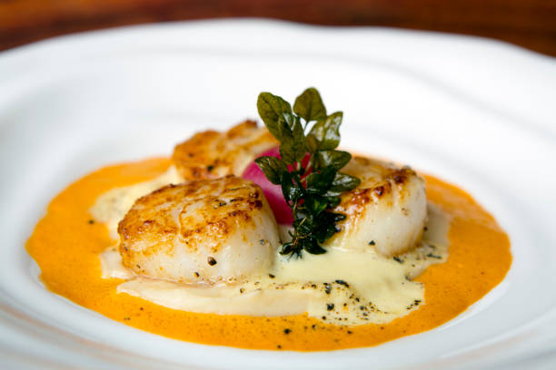 Seared Pan Fried Scallops Seared pan fried scallops with a red pepper cream sauce and hollandaise sauce served on a white plate with thyme garnish. mollusca stock pictures, royalty-free photos & images