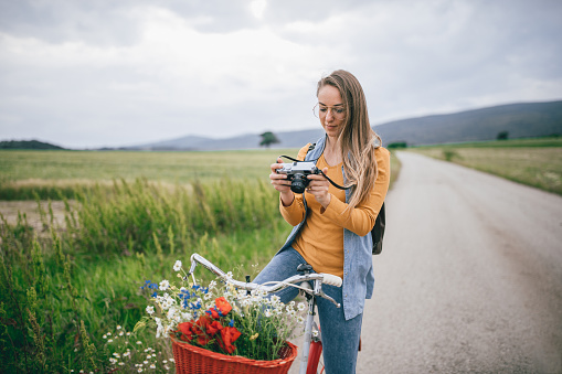 Young woman riding a bike through the countryside and taking photos of beautiful landscape