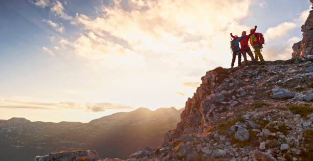 Rear view of male and female mountaineers celebrating victory on top of mountain at sunset.
