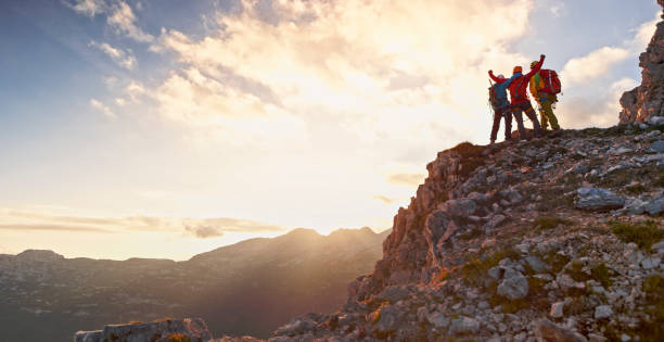 Mountaineers celebrating victory Rear view of male and female mountaineers celebrating victory on top of mountain at sunset. mountain peak stock pictures, royalty-free photos & images