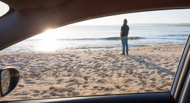 istock View past car window to man with hands in pockets, at beach 964276228