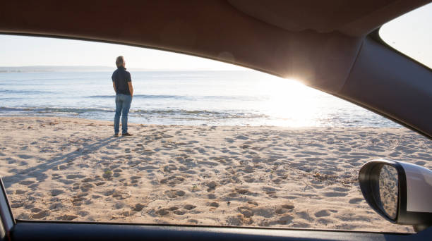 istock View past car window to man with hands in pockets, at beach 964276244