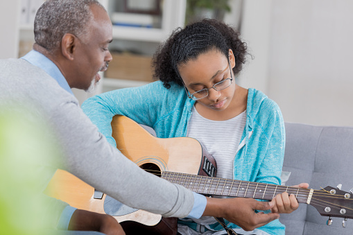 Confident African American senior man gives teenage girl guitar lessons.