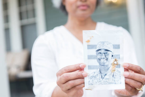 Senior woman holds photo of army son Sad African American senior woman holds a black and white photo of her son who is serving overseas on a military assignment. proud army mom stock pictures, royalty-free photos & images